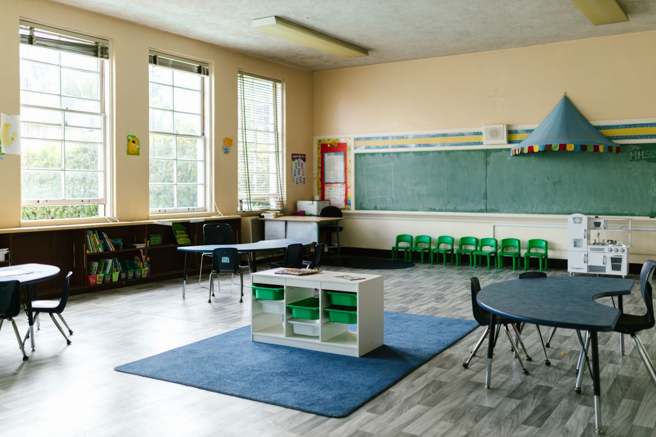 services-03 Spacious preschool classroom interior with tables, chairs, and a chalkboard for a learning environment.
