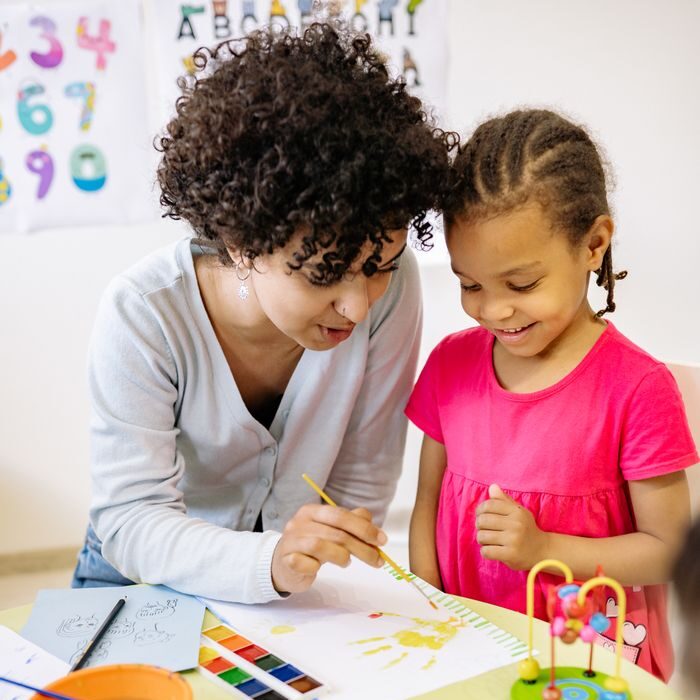 Programs A teacher assists a child with painting, promoting creativity in an educational setting.